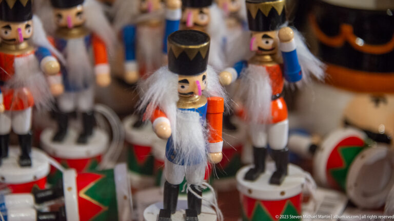 Painted wooden nutcracker soldiers with black hats, white beards, colorful uniforms, and round bases in a market display.