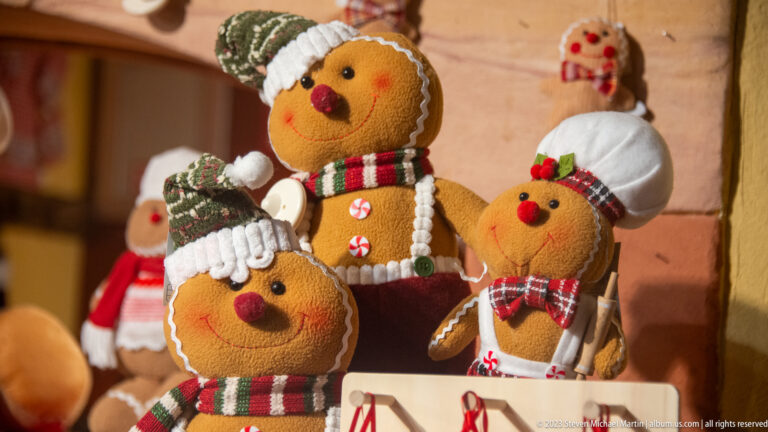 Plush gingerbread characters wearing knitted hats, scarves, and plaid ribbons on a Christmas-market display.