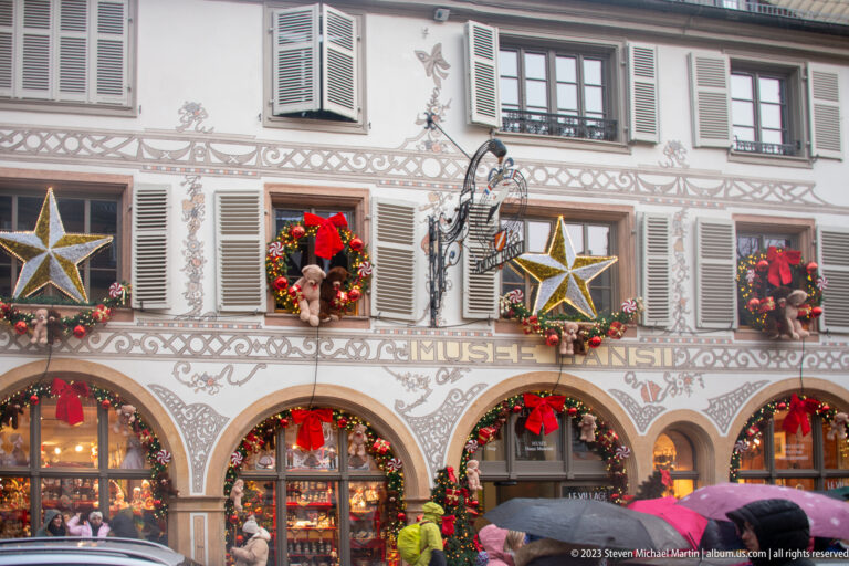Musée du Jouet façade decorated with large stars, wreaths, garlands, red bows, painted scrollwork, and arched windows.