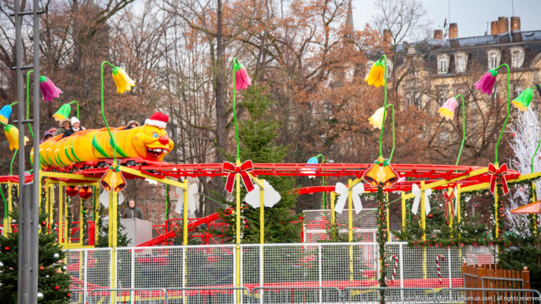 Colorful caterpillar amusement ride on a red track among oversized flower decorations and bare winter trees.