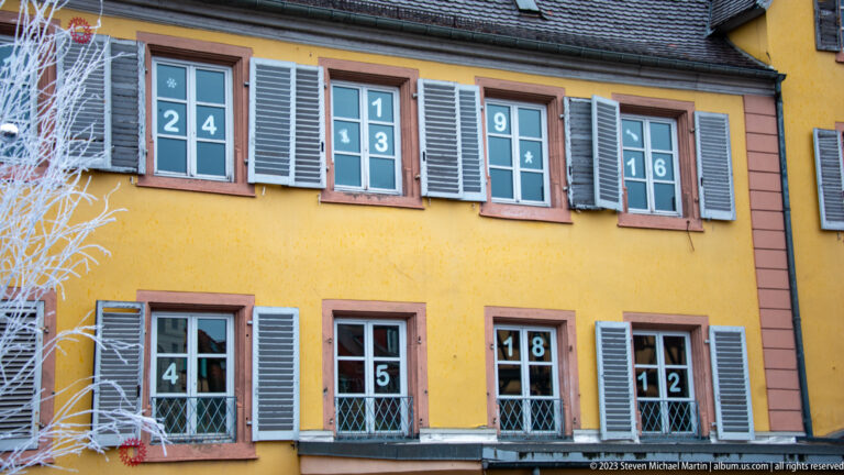 Yellow house with gray shutters and numbered window panes arranged as an Advent-calendar display.