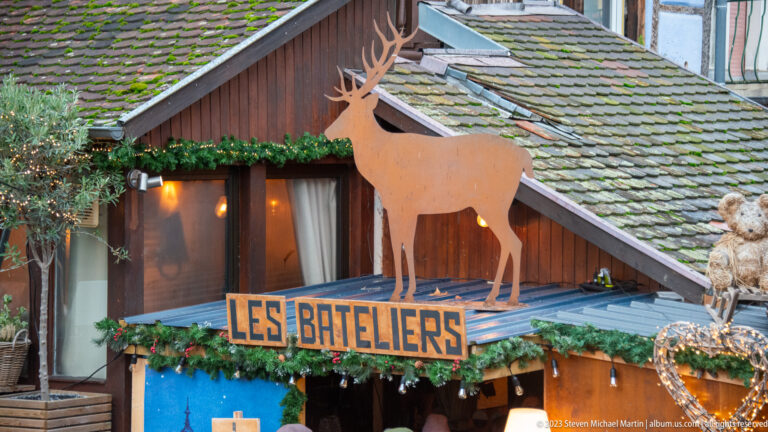 Wooden Les Bateliers sign beneath a cutout deer on a chalet-style façade decorated with evergreen garland.
