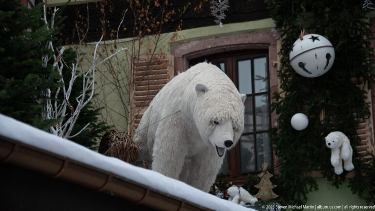 Large white polar-bear decoration beside evergreen garlands, oversized bells, ornaments, and a smaller bear figure.