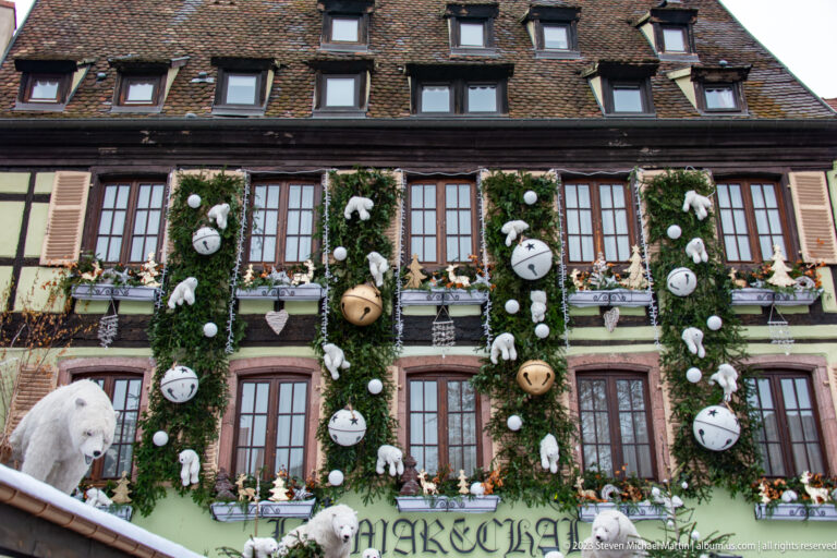 Historic façade covered in vertical evergreen garlands, oversized bells, round ornaments, and polar-bear figures.
