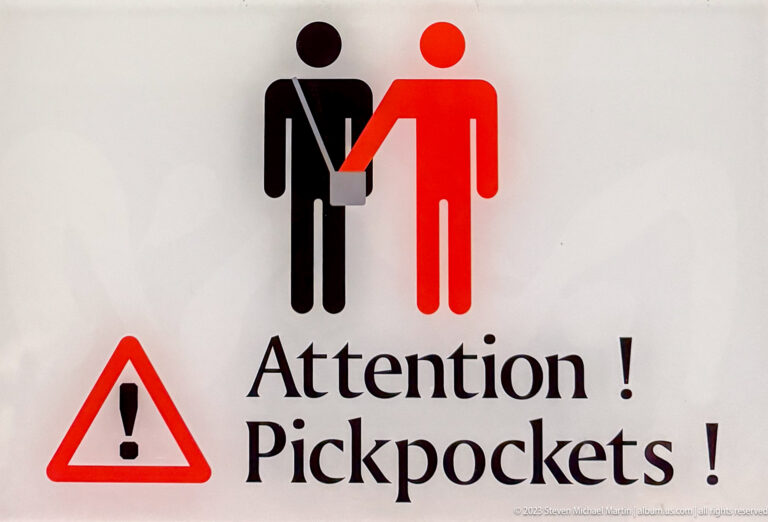 Warning sign reading Attention! Pickpockets! with red-and-black figures and a triangular exclamation symbol.