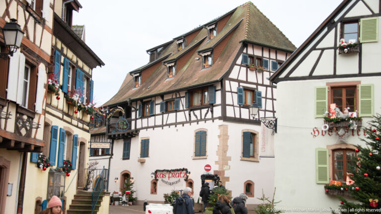 Half-timbered houses with colorful shutters and Christmas decorations around a small street junction with visitors.