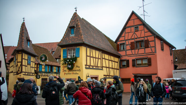Winter crowd before yellow and orange half-timbered houses decorated with wreaths and Christmas greenery.