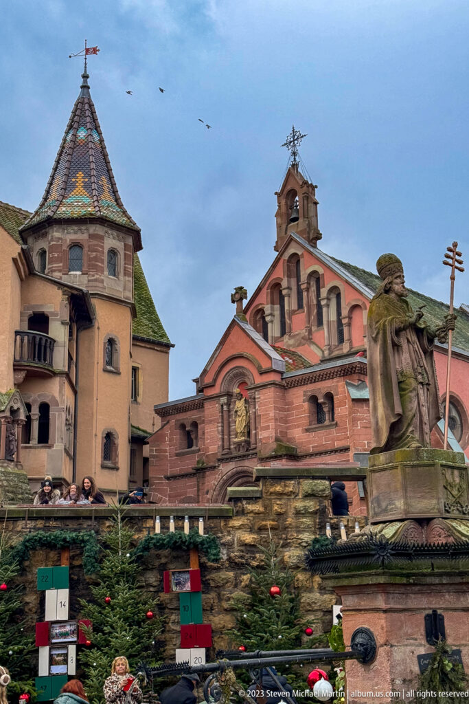 Saint Leo IX fountain monument before the Château Saint-Léon complex, surrounded by decorated Christmas trees.