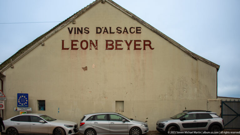 Plain gable wall marked Vins d’Alsace Léon Beyer above several parked cars.