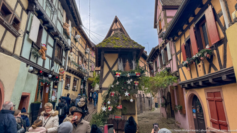 Visitors walk along a narrow lane of half-timbered houses beside a Christmas tree decorated with stars.