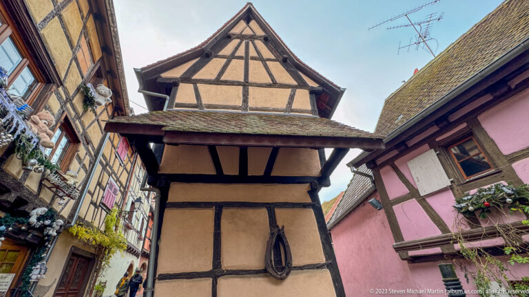Low-angle view of a narrow half-timbered house with a projecting upper story and steep tiled roof.