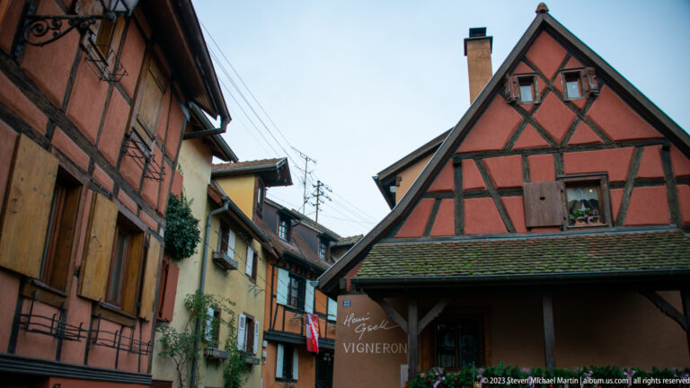 Gabled half-timbered Vigneron building at the end of a narrow street lined with shuttered historic houses.