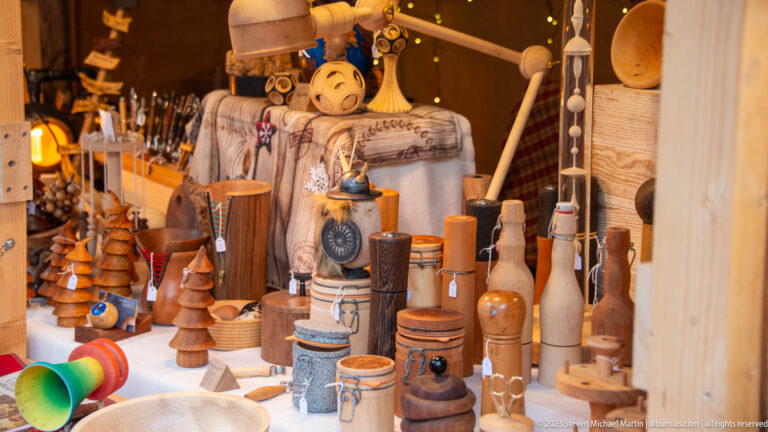 Christmas market stall filled with turned wooden mills, cups, utensils, small trees, carved figures, and other woodcraft.