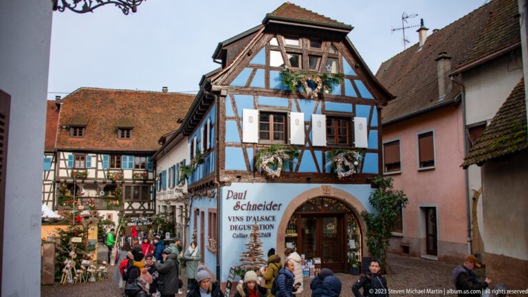 Visitors crowd a narrow street outside the blue-and-white Paul Schneider Vins d’Alsace half-timbered shop.