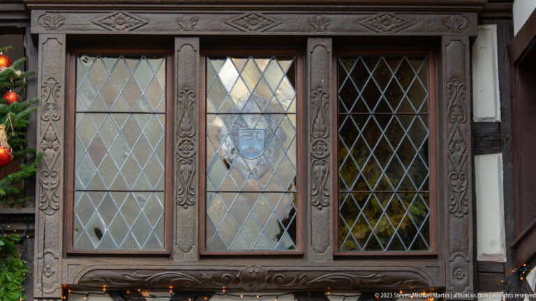 Three diamond-paned windows framed by dark carved wood with floral and geometric ornament.