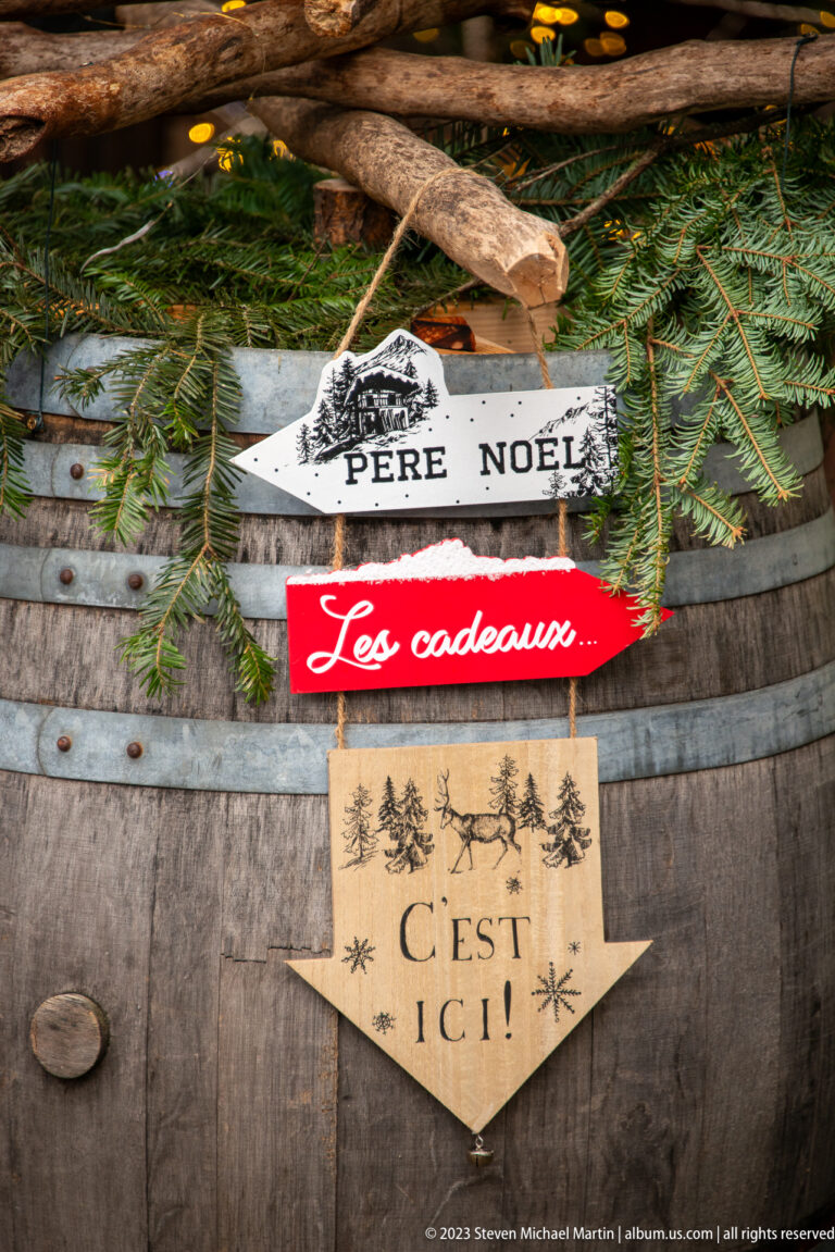 Wooden wine barrel with evergreen and signs reading “Père Noël,” “Les cadeaux,” and “C’est ici.”