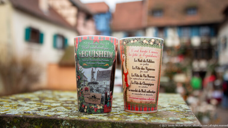Two decorated souvenir cups, one labeled Eguisheim and the other listing Alsatian wine-route villages.