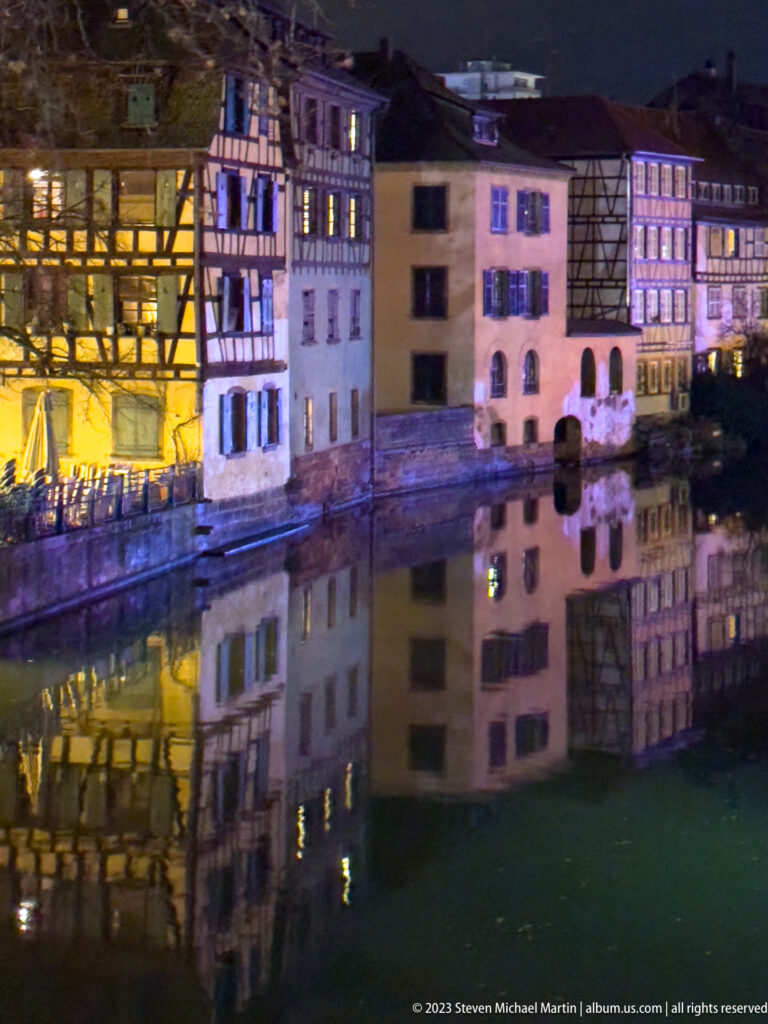 Historic Petite France houses in warm and purple light reflected almost symmetrically in a calm canal.
