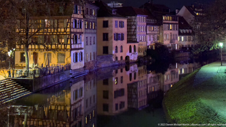 Historic Petite France houses reflected in a canal beside a dark grassy bank at night.