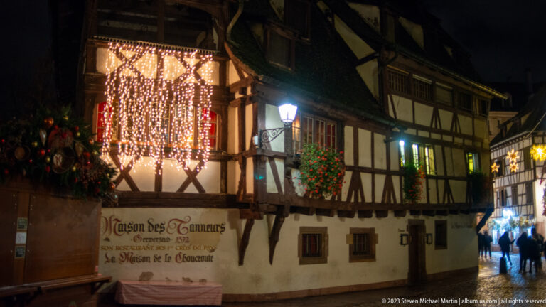 Maison des Tanneurs half-timbered façade with its 1572 inscription, Christmas lights, wreaths, and greenery.