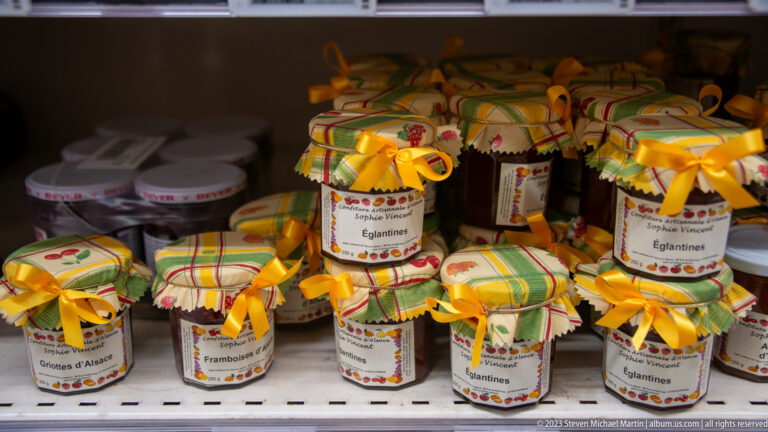 Small jars of fruit preserves with checked fabric lids and yellow bows, including labels for Eglantines and Framboises.