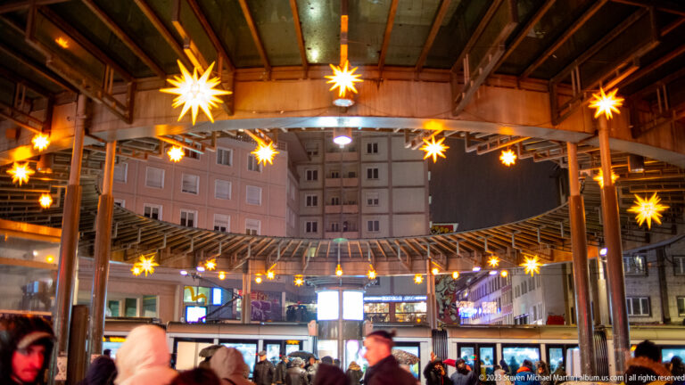 Covered timber market pavilion with glowing star lights overhead and visitors gathered beneath.