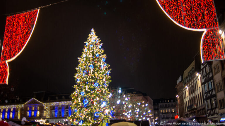Place Kléber Christmas tree centered between large red illuminated panels, with a smaller white-lit tree nearby.
