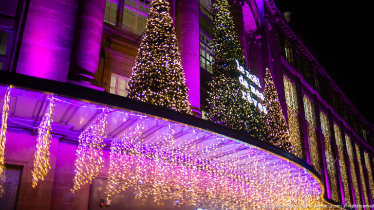 Christmas trees and multicolored illumination above a cascading light canopy on the Galeries Lafayette façade.