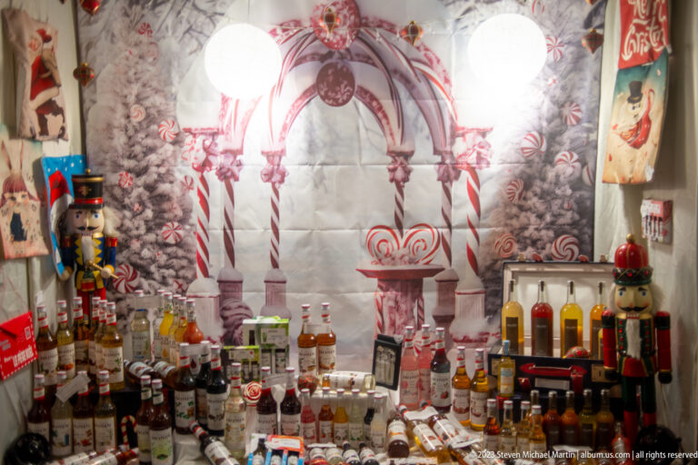 Shop window filled with bottles, nutcracker figures, candy-cane decorations, and snowy Christmas graphics.