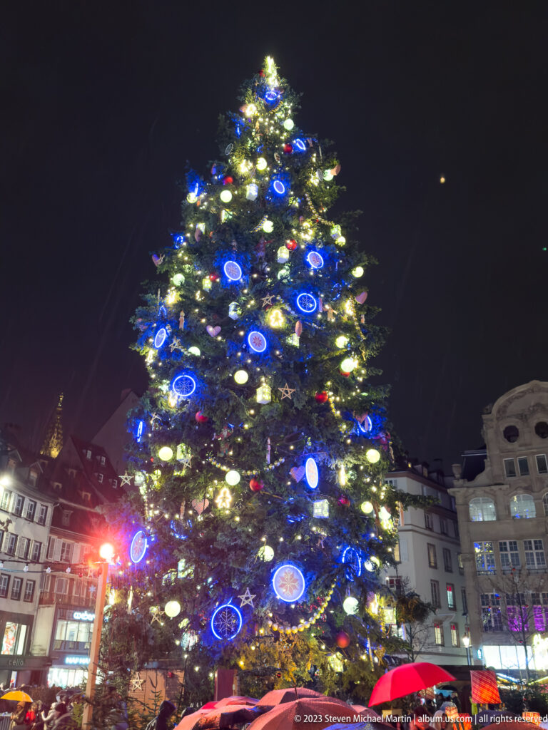 Low-angle view of Place Kléber’s illuminated Christmas tree with blue and red ornaments at night.