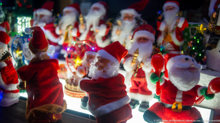 Dense display of Santa Claus figurines in red suits and white beards at a brightly lit Christmas-market stall.