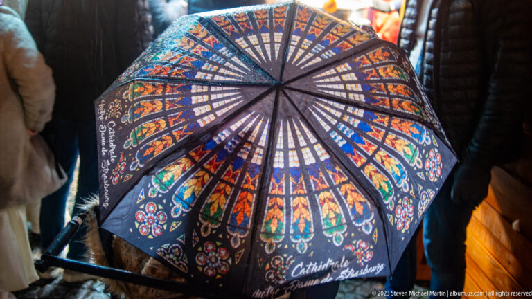 Open umbrella printed with colorful stained-glass patterns and the words “Cathédrale Strasbourg.”