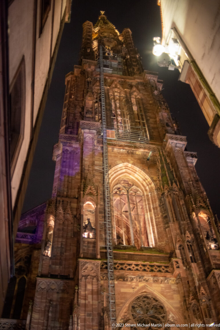 Low-angle Strasbourg Cathedral detail with pointed-arch window, sculpted portal, Gothic carving, and tower above.