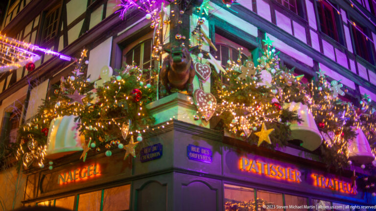 Christmas-covered pâtisserie on Rue des Dentelles with stars, gingerbread figures, garlands, and half-timbered upper stories.