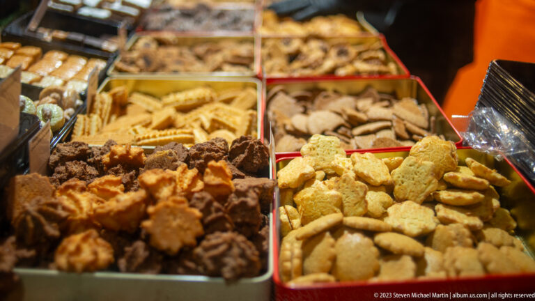 Metal trays filled with assorted small Christmas biscuits in pale, chocolate-coated, and darker varieties.