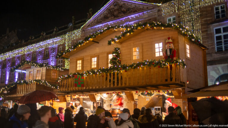 Two-story wooden Christmas chalet with garlands, gift decorations, nutcracker figure, and crowded counter below.
