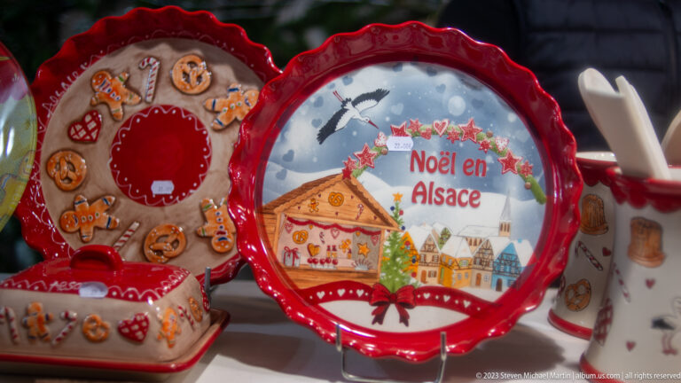 Red-edged ceramic plate reading “Noël en Alsace,” illustrated with a gingerbread house and winter village.