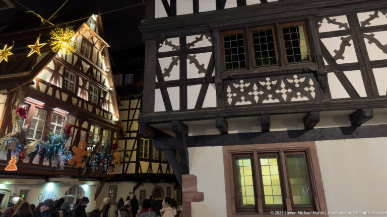 Close view of half-timbered façades, one decorated with stars, garlands, and gingerbread figures for Christmas.