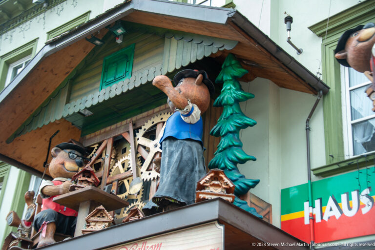 Decorative shopfront with large carved figures, miniature chalet details, evergreen motifs, and colorful signage.