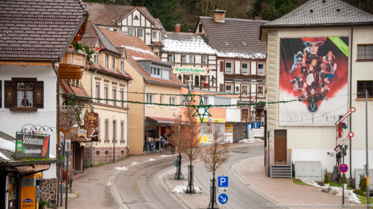 Curving Triberg street lined with shops and traditional buildings beneath a wooded Black Forest hillside.
