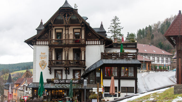 Hotel Pfaff rising along a sloping Triberg street, with ornate balconies, neighboring buildings, and patches of snow.
