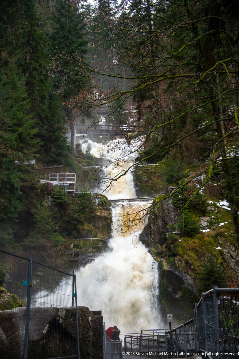 Triberg Waterfalls descending in broad foaming cascades through evergreen forest, with visitor railings beside the ravine.