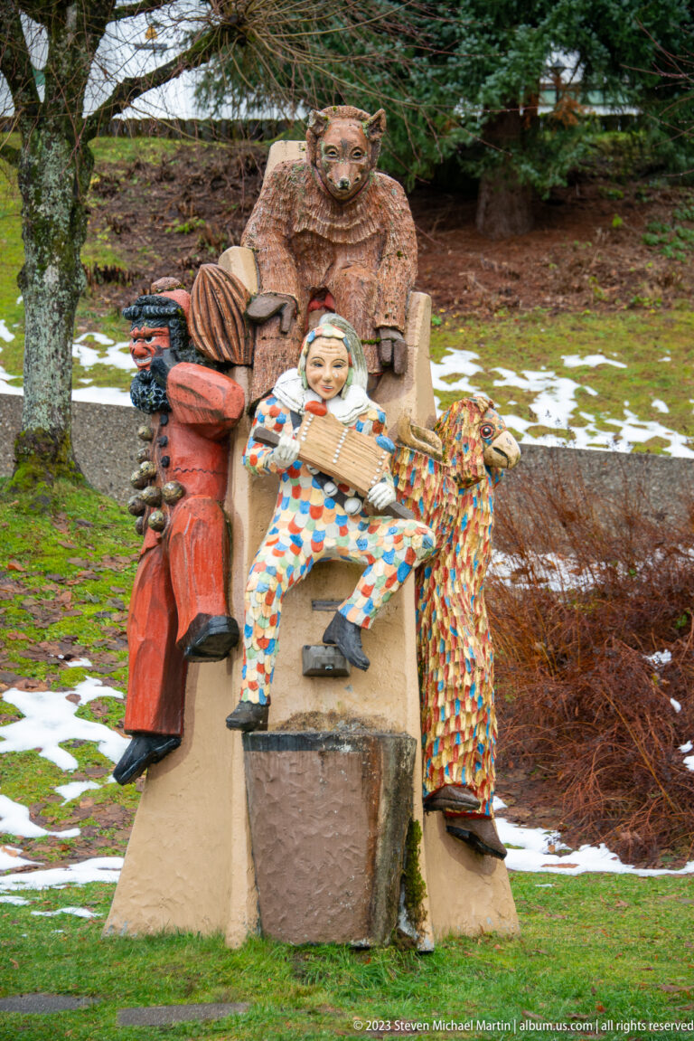 Outdoor sculpture group with a bearded seated figure and smaller figures in colorful patterned costumes.