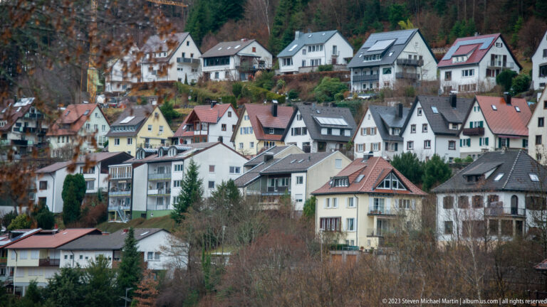 Closely packed houses with varied pitched roofs climbing a wooded hillside in the Black Forest.