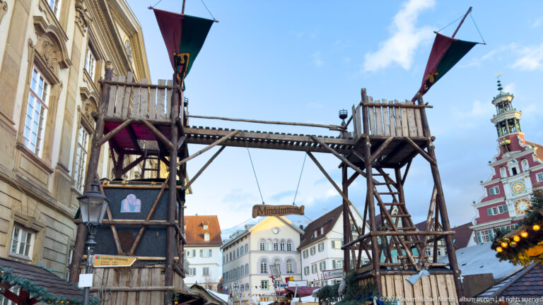 Tall wooden market structure with ladders, platforms and flags, with Esslingen's Altes Rathaus at right.