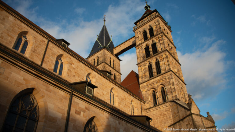 Low-angle view of the twin towers of Stadtkirche St. Dionys joined by an elevated bridge above the stone nave.
