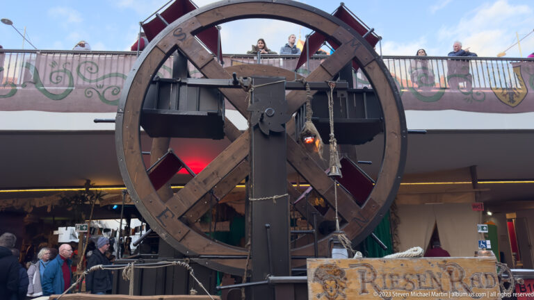 Large wooden wheel in a heavy timber frame with chains and metal fittings at the medieval market.