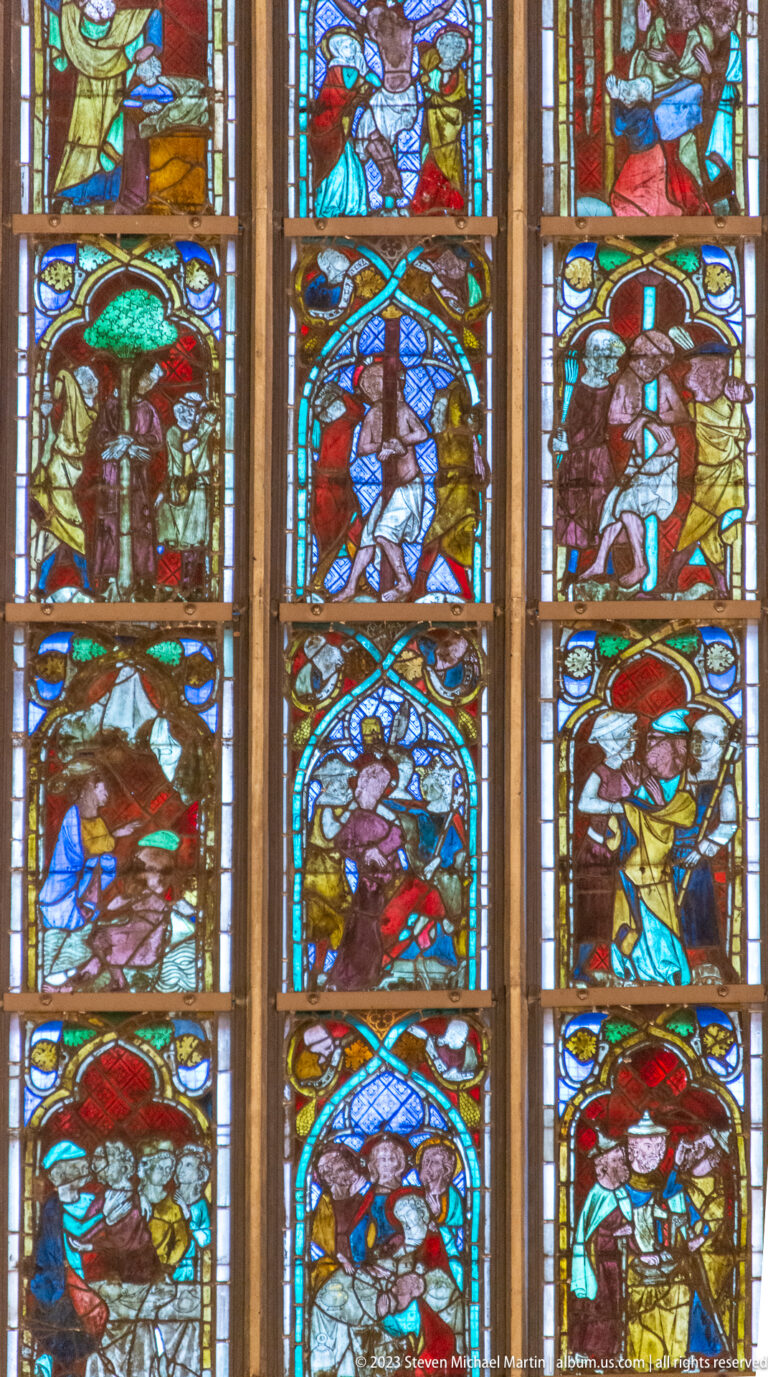 Close view of colorful figurative stained-glass panels with robed figures, angels, and repeated arched borders.