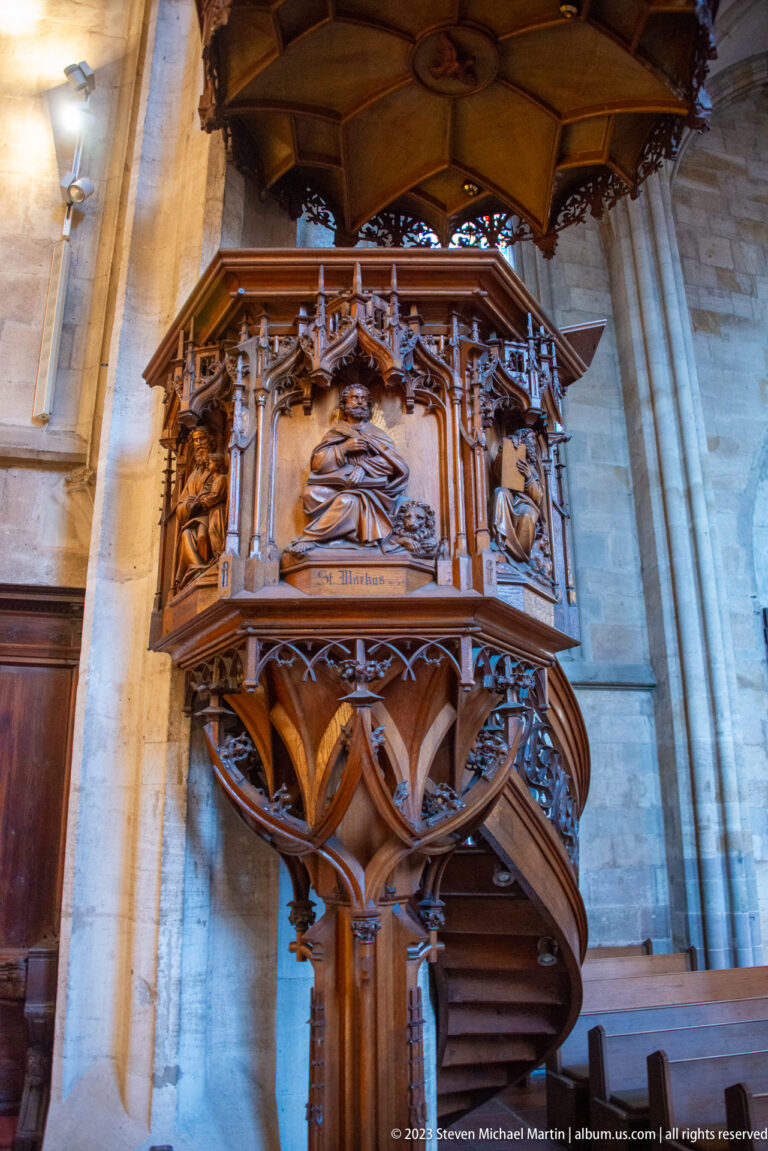 Ornate carved wooden pulpit with relief panels, tracery, curved stair, clustered support, and broad sounding board.