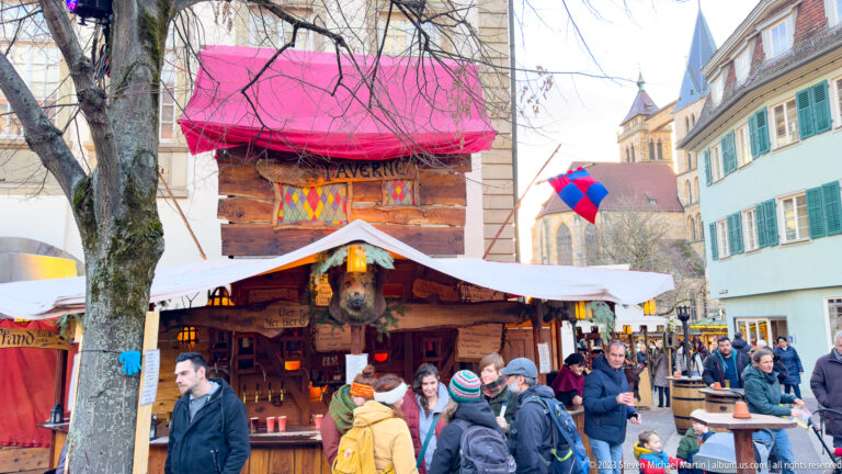 Crowded rustic tavern stall with red canopy, heraldic decorations and a carved animal head in Esslingen.